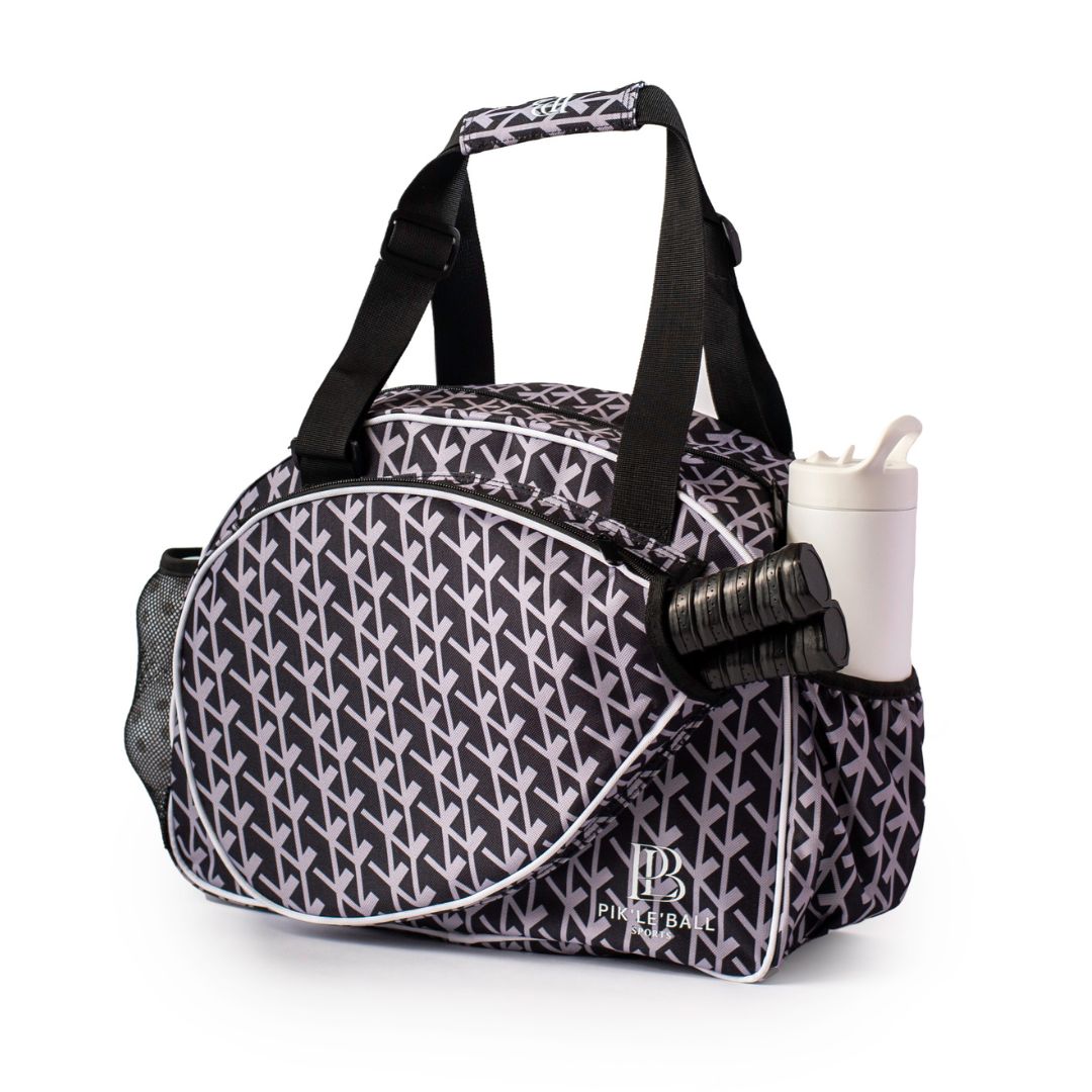 The Pik'le'Ball Sports Court Couture Black Premium Women's Pickleball Bag features a black-and-white geometric design, black handles, side pockets for a white water bottle and a black item, plus a front pocket with "PICKLEBALL" and paddle logo.