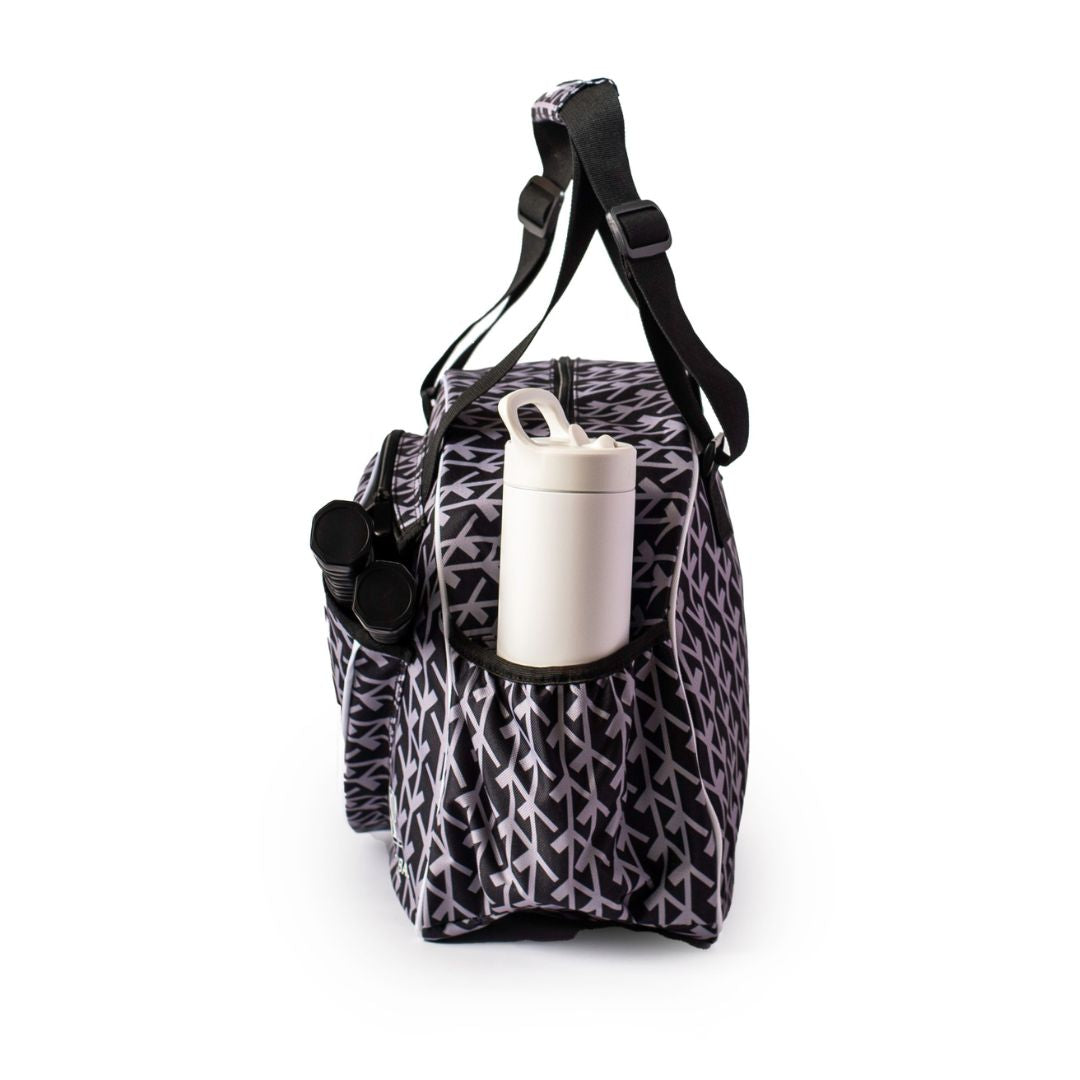 The Pik'le'Ball Sports Court Couture Premium Women's Pickleball Bag features a black and white geometric leaf design, adjustable black straps, multiple compartments, a paddle sleeve, and a side pocket for your water bottle.