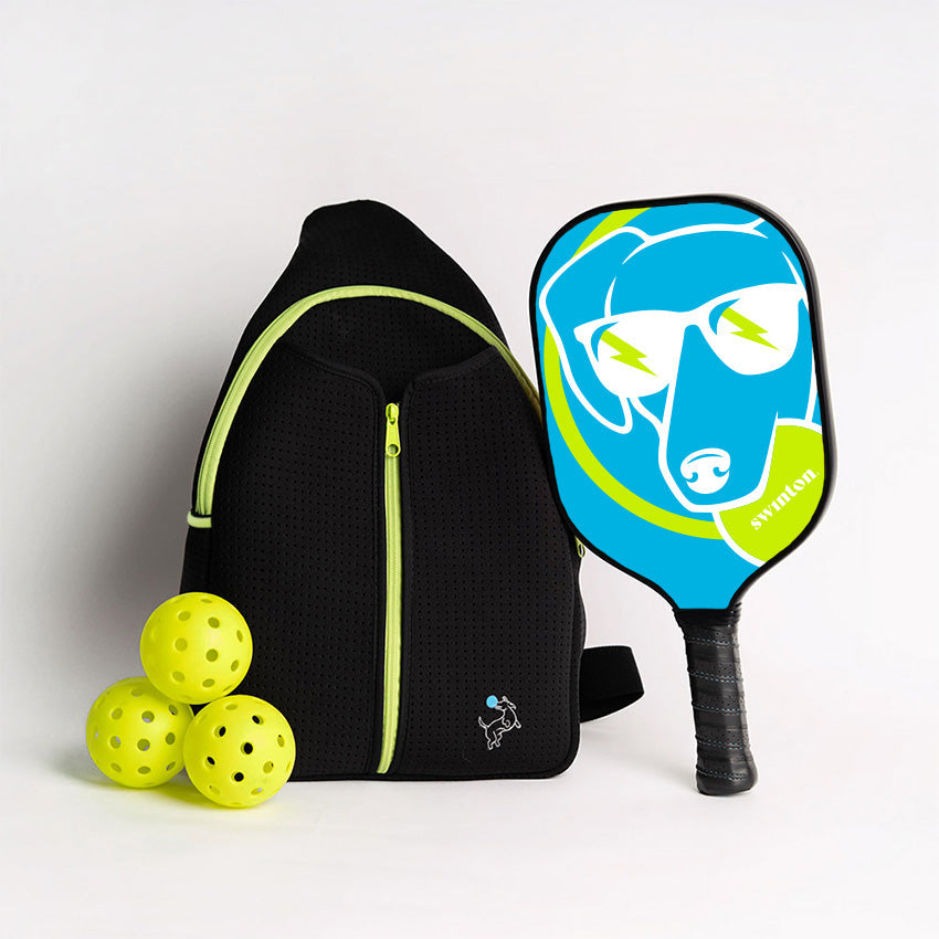 The Swinton Pickleball Starter Bundle - Black Sling Bag Combo includes a black sports backpack with lime accents, three yellow pickleballs, and a dog-themed blue and lime paddle—making it the perfect pickleball gift.