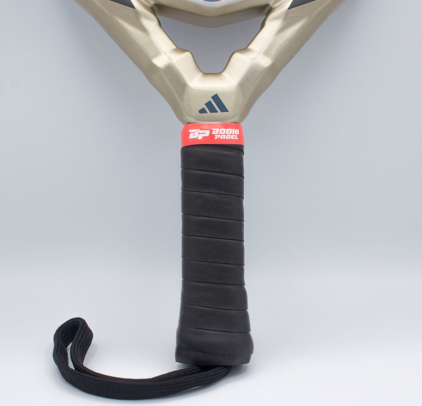 Close-up of a paddle racket handle wrapped in Bodhi Performance PROtack™ Premium Padel Overgrips for superior moisture absorption, featuring a black textured grip, red “Pdooh Proel” band, gold frame, blue logo, and black strap on gray background.