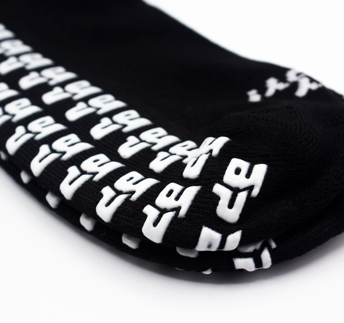 Close-up of the bottom of Bodhi Performance’s Performance Socks - GRIPtech™ showing white “Y”-shaped silicone grips. The neatly stacked socks display textured patterns designed to help prevent slipping, set against a white background.