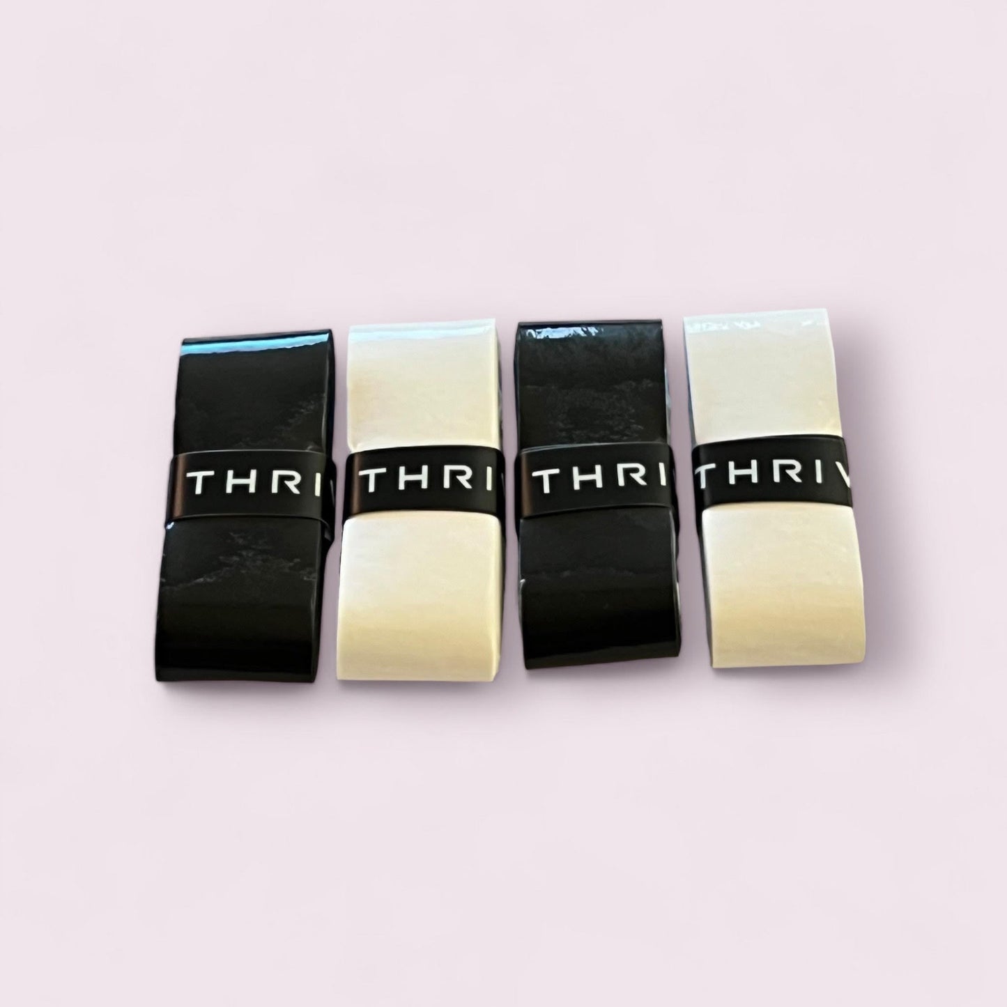 Four rectangular overgrips stand upright in a row against a pale pink background. Each features the bold “THRIV” text, echoing the signature look of Thrive Pickleball’s Overgrips (Super Tacky), known for exceptional tack and durability.