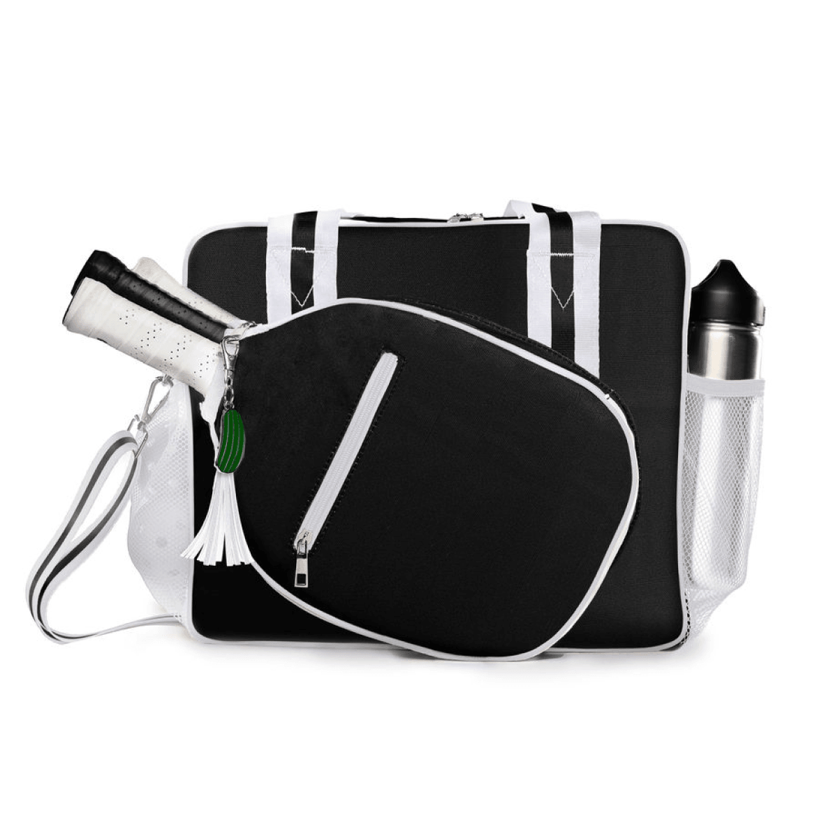 The Fresh Pickle Lola Pickleball Tote Bag in black and white stands upright with dual straps, a side pocket holding a water bottle, a racket compartment with handle visible, plus a white tassel and green keychain on the zipper.