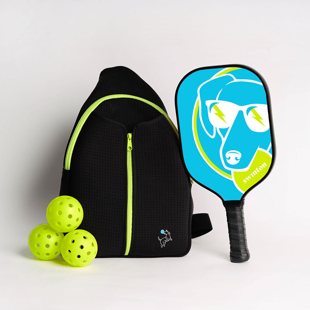 A black backpack with neon yellow zippers, three neon yellow pickleballs, and the Swinton Pickleball Hero Blue Dog Paddle—a lightweight graphite paddle featuring a blue background and a dog in sunglasses with yellow lightning bolts.
