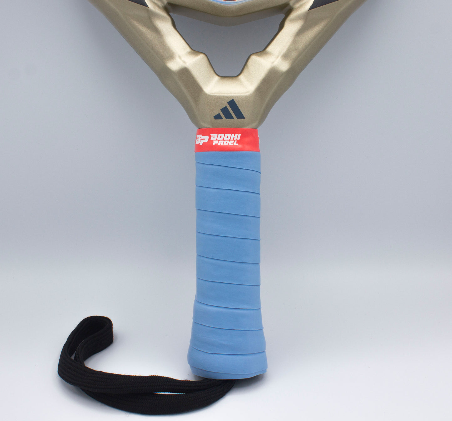 A close-up of a gold padel racket handle wrapped in Bodhi Performance PROtack™ Premium Padel Overgrips in light blue, featuring a red “300H PADEL” label on top and a coiled black wrist strap at the base for secure play.