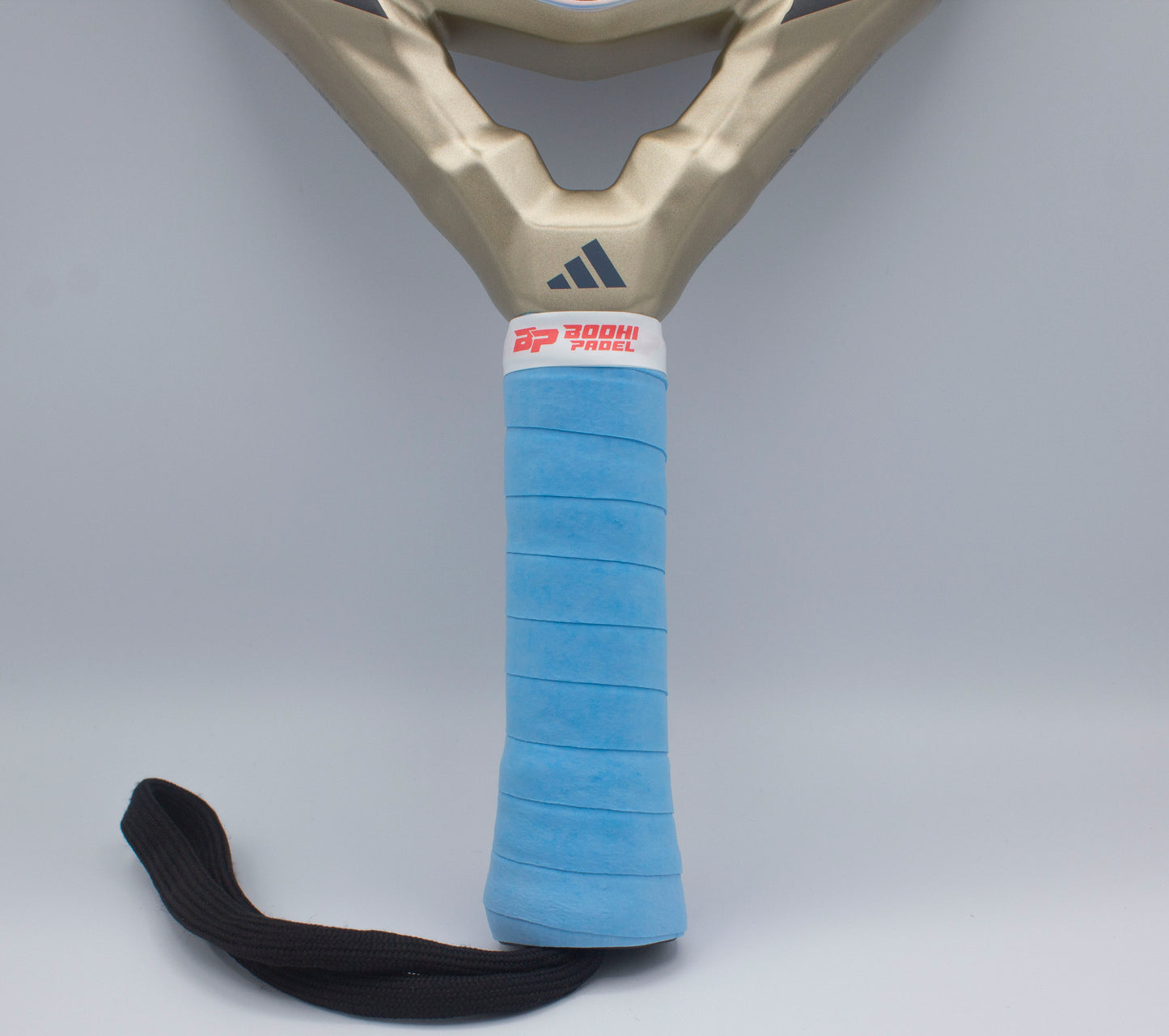 Close-up of a padel racket handle wrapped with Bodhi Performance’s DRYtack™ Premium Padel Overgrip in blue for moisture control, featuring a black wrist strap and a white label, metallic gold upper section, against a light gray background.