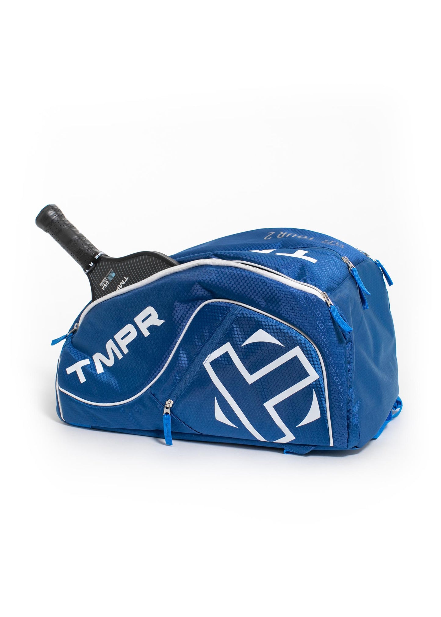 A blue TMPR Sports Tour 2 Backpack with white accents and a bold logo lies on its side, revealing a black pickleball paddle in the side pocket. This spacious backpack includes multiple zippered compartments.