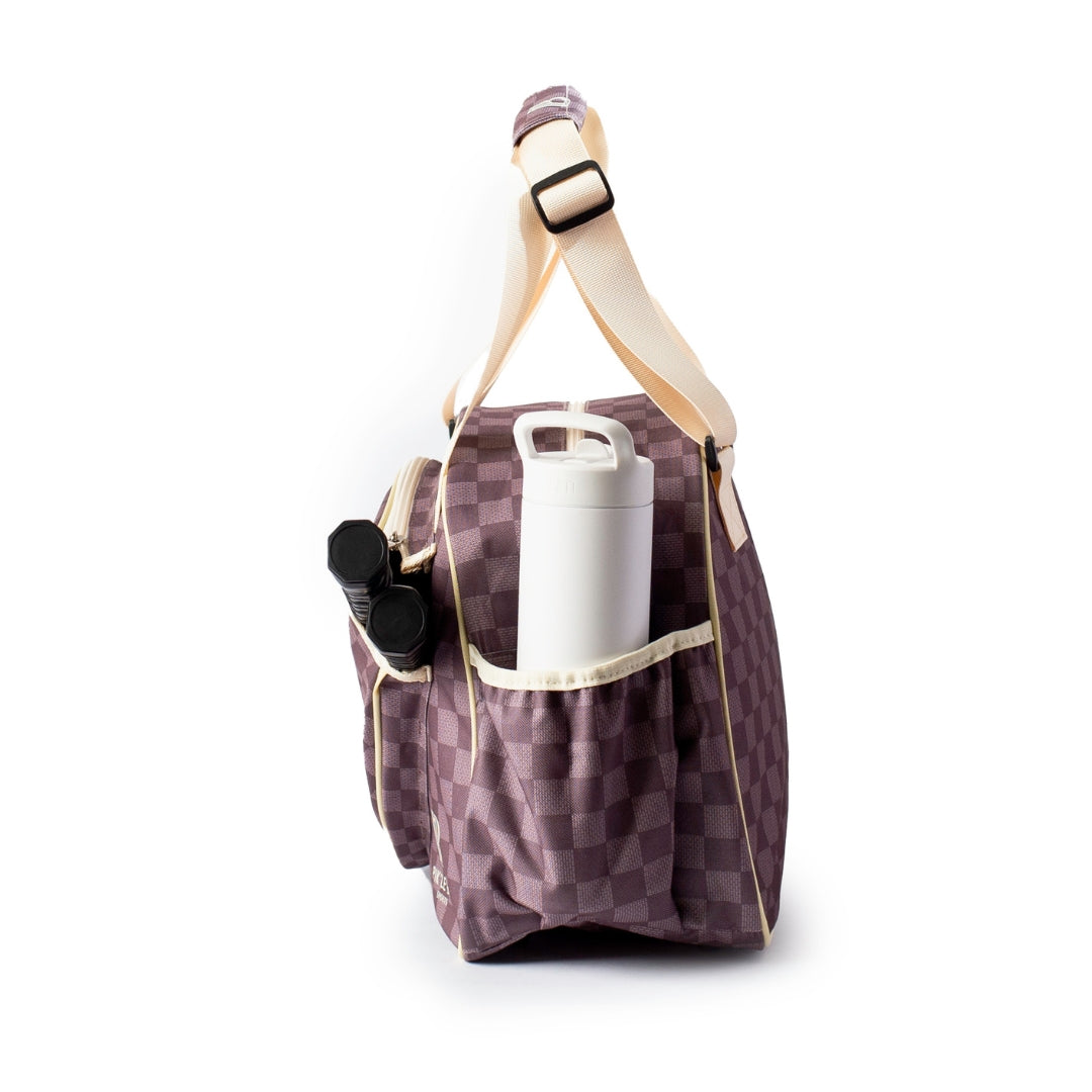A side view of the Pik'le'Ball Sports Checkered Chic Premium Women's Pickleball Bag with cream straps is shown. The stylish bag features a side pocket holding a white water bottle and a black item, set against a plain white background.