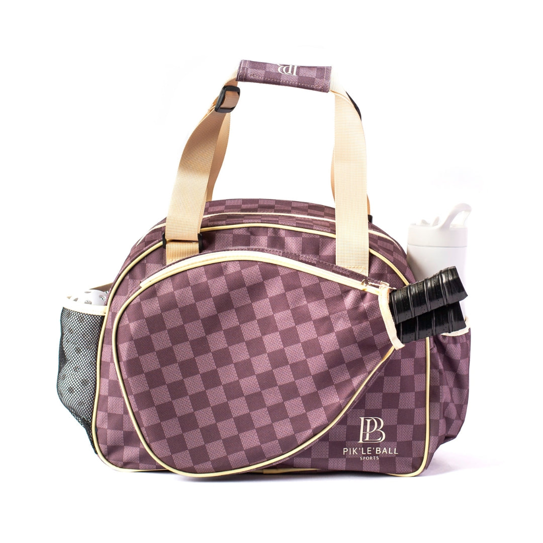 The Pik'le'Ball Sports Checkered Chic Brown Premium Women's Pickleball Bag features beige handles, a racquet-shaped front pocket with a black paddle, mesh side pocket with a white water bottle, and the logo on the lower right corner.