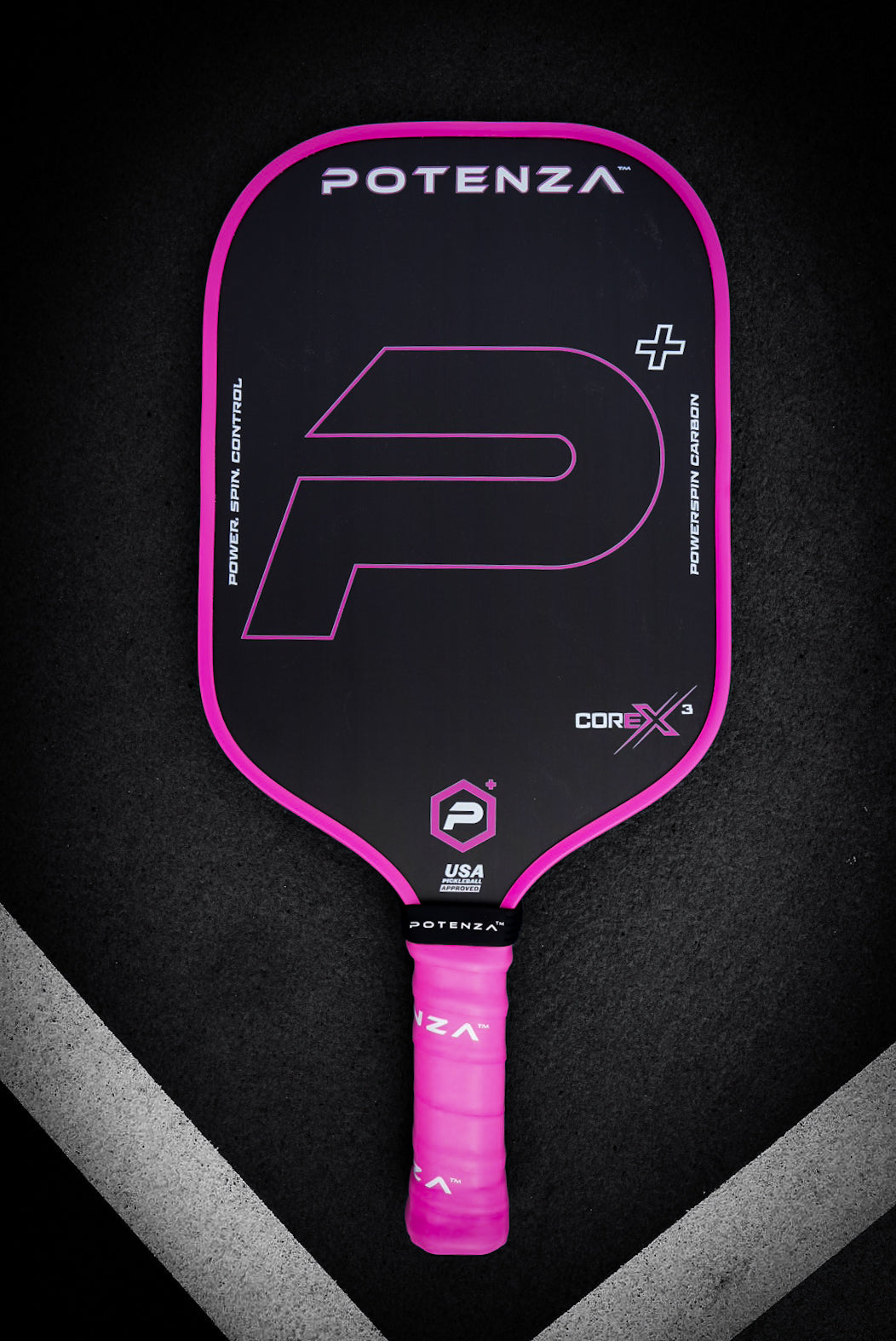 The Potenza Pickleball P+ PowerSpin Carbon COREx3 (Neon Pink, Elongated Face) features a black carbon fiber paddle with bold neon pink edges, grip, and accents, plus a large stylized P+ on the face. It sits on a black surface with white V-shaped lines below.