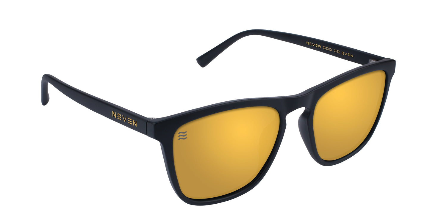 A pair of Neven Eyewear Liquid Gold sunglasses, featuring black frames and gold mirrored lenses. "NEVEN" is in gold on the left arm; inside the right arm reads “NEVER COAST OR EVEN.” Part of the Cambridge collection.