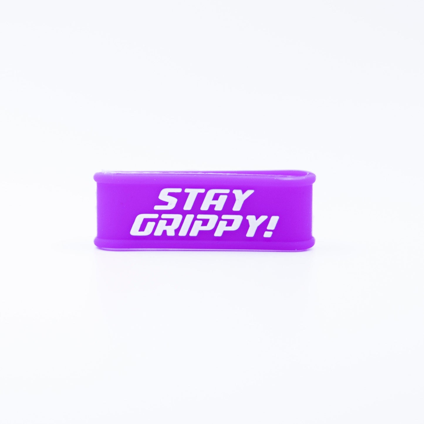 A small, rectangular purple silicone Paddle Band by Bodhi Performance lies on a white background. Its front displays bold white uppercase text reading “STAY GRIPPY!” The minimalistic composition is brightly lit.