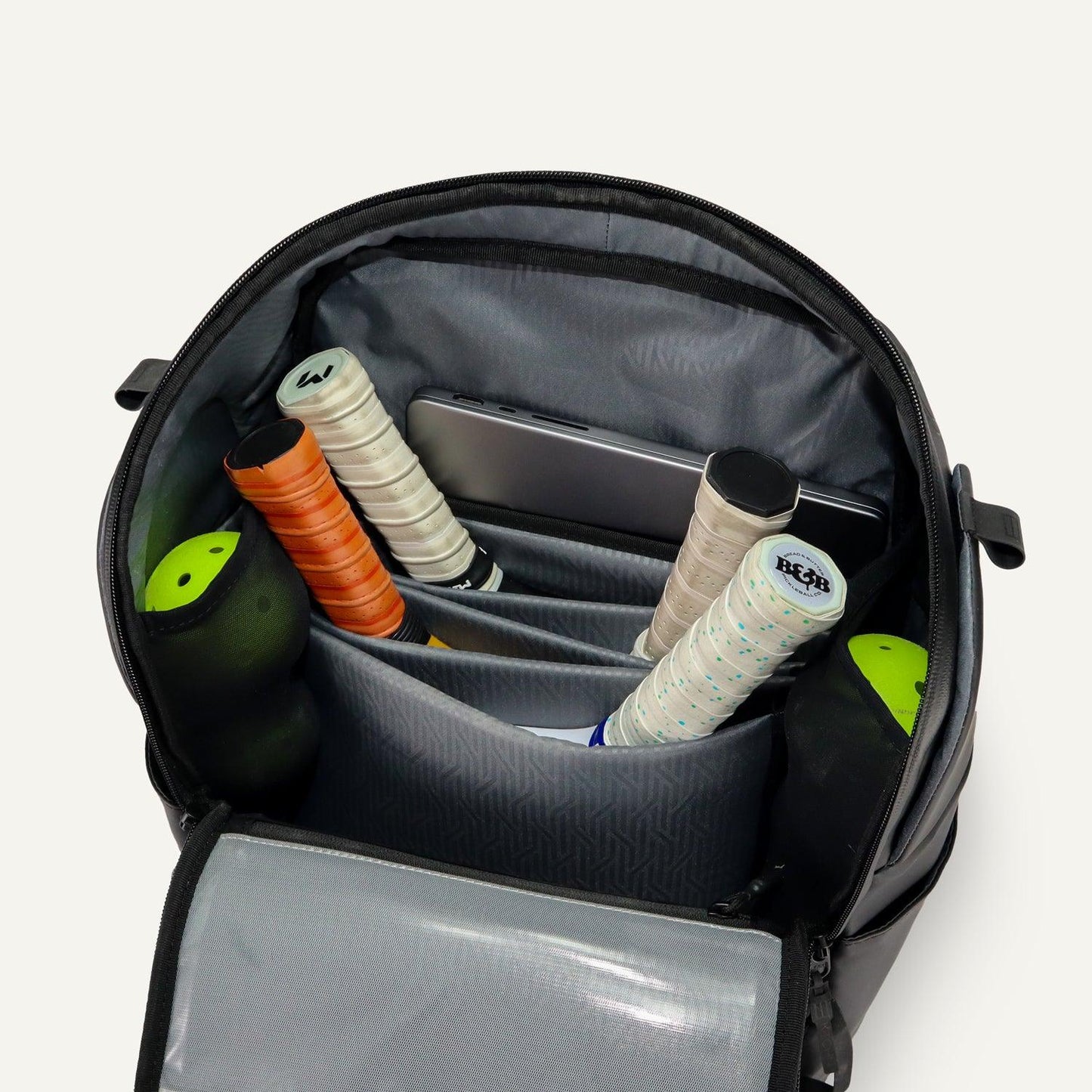 A top-down view of the FORWRD Court Caddy Pickleball Bag reveals its modular design—neatly storing four racquets with colorful grips, a laptop in a padded sleeve, and two green-capped tennis ball containers in side pockets.