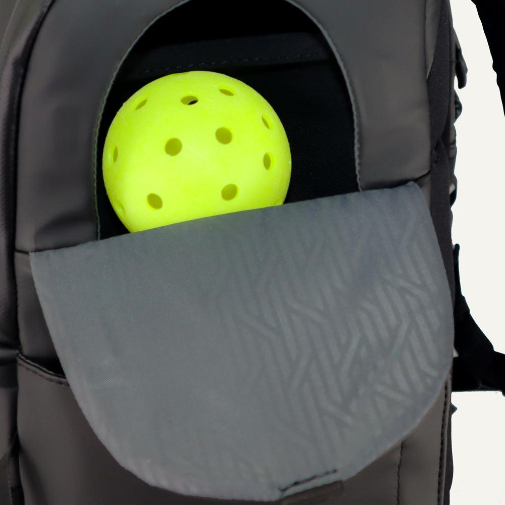 A fluorescent yellow pickleball peeks from the partially open front pocket of a FORWRD Court Caddy Pickleball Bag, its black exterior and gray, geometric-patterned flap set against a plain white background.