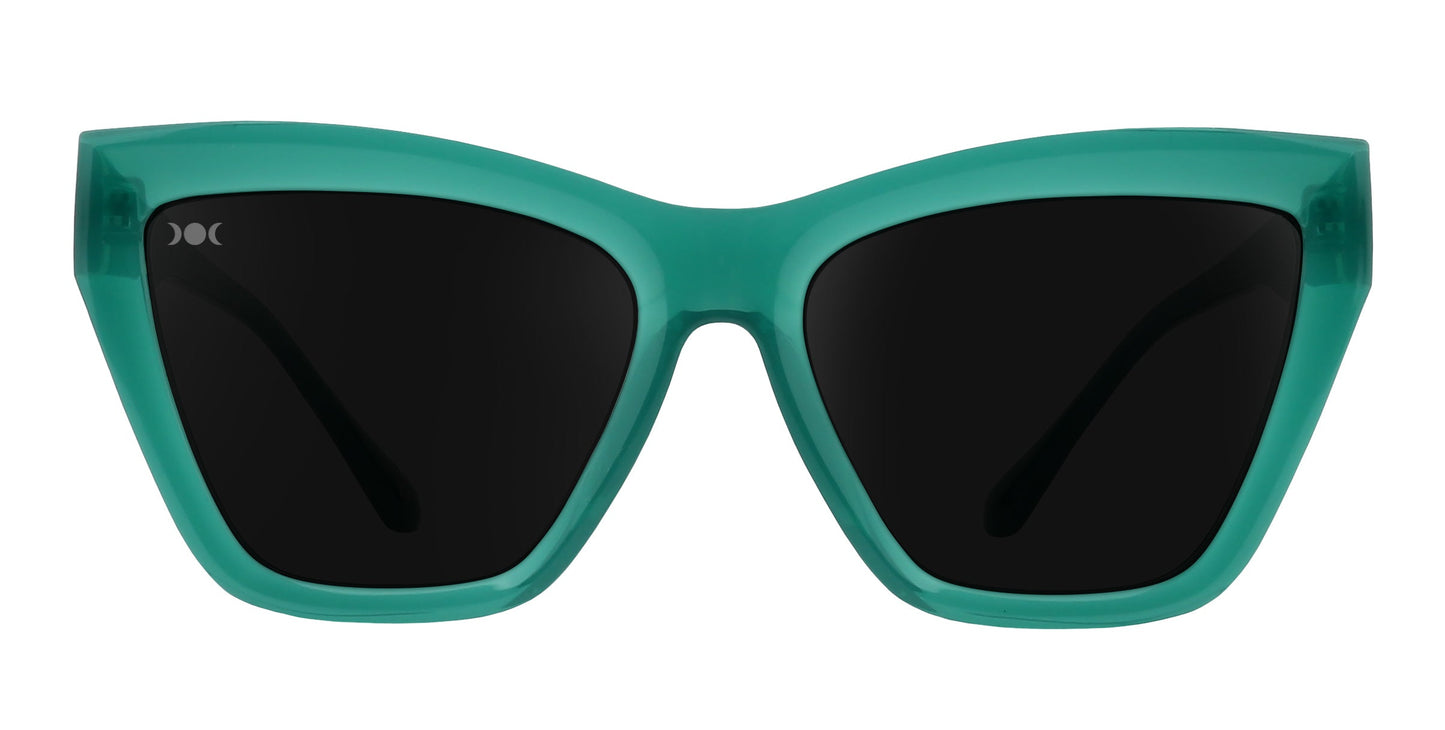 The Neven Eyewear Iris sunglasses feature thick, glossy teal-green cat-eye frames and large black lenses. This bold, angular style offers polarized UV400 protection and is shown front-on against a plain white background.