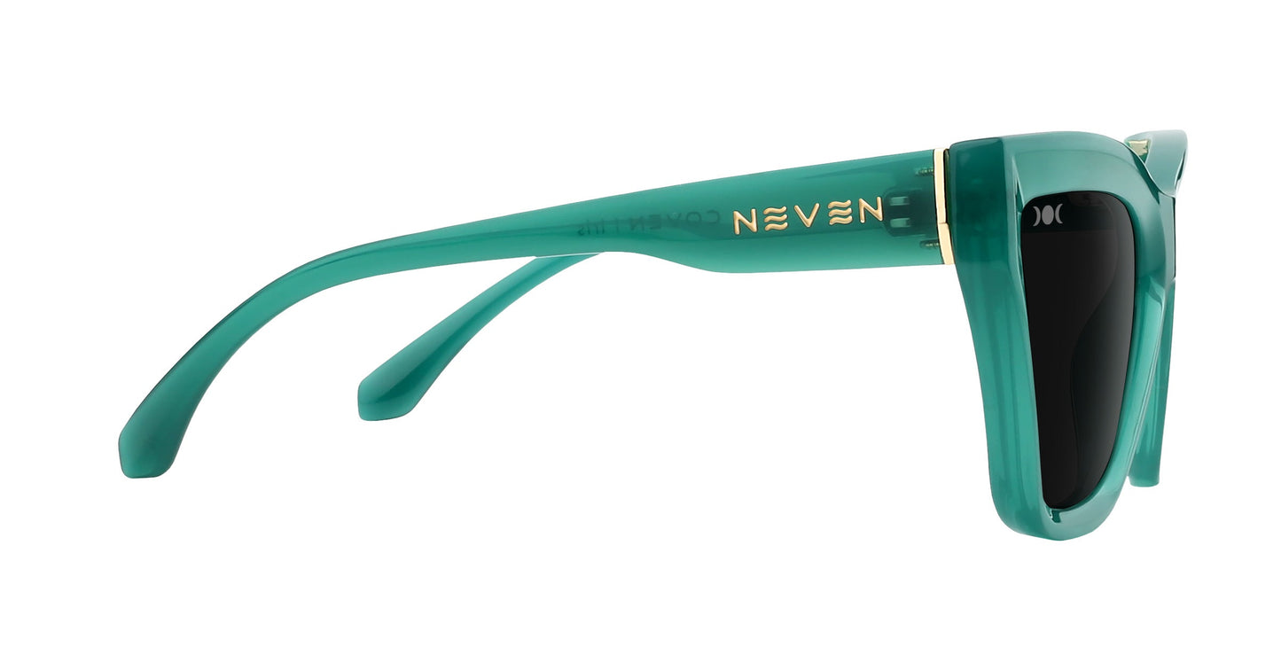 Side view of Iris by Neven Eyewear: glossy teal statement sunglasses with thick frames, dark lenses, gold accents, and "NEVEN" in gold on the arm near the hinge. The bold, chunky shape gives these shades a modern edge.