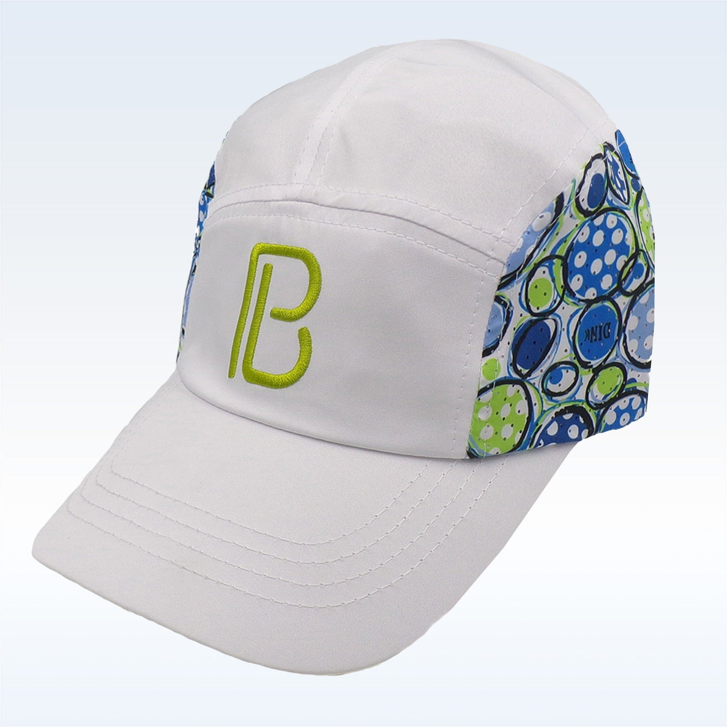 The PB Cap Dink 1 by Pickleball Bella is a white adjustable velcro cap with a lime green PB logo, blue/green/white abstract bubble side panels, visible brim stitching, and a soft fabric structure. Displayed on a light gradient background.