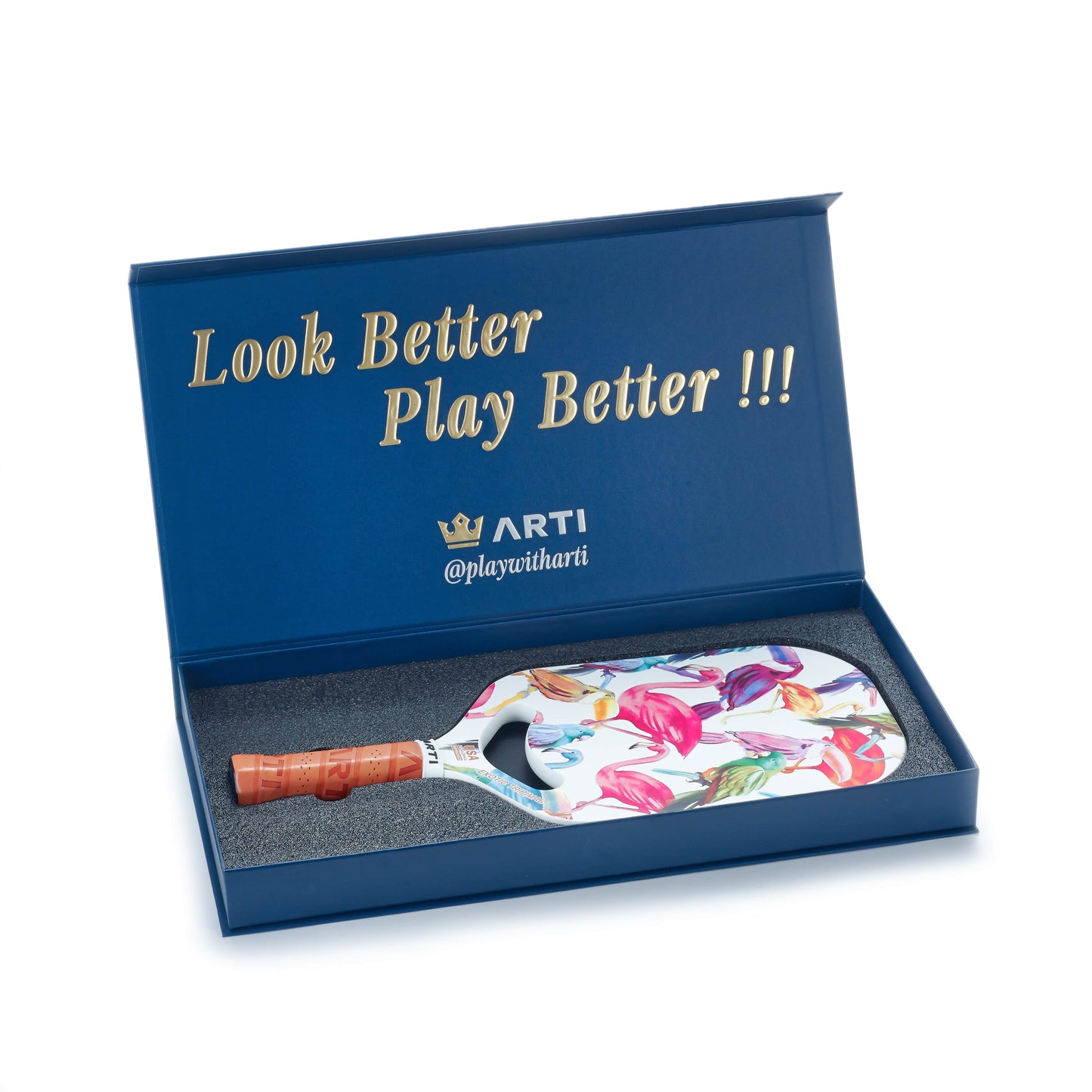 A blue box with gold lettering holds the ARTI Carbon Fiber EXOTIC TRIPIMAL "Flamingo" USAPA-approved pickleball paddle featuring a floral pattern and brown grip. The lid displays the ARTI brand and handle “@playwitharti.”.