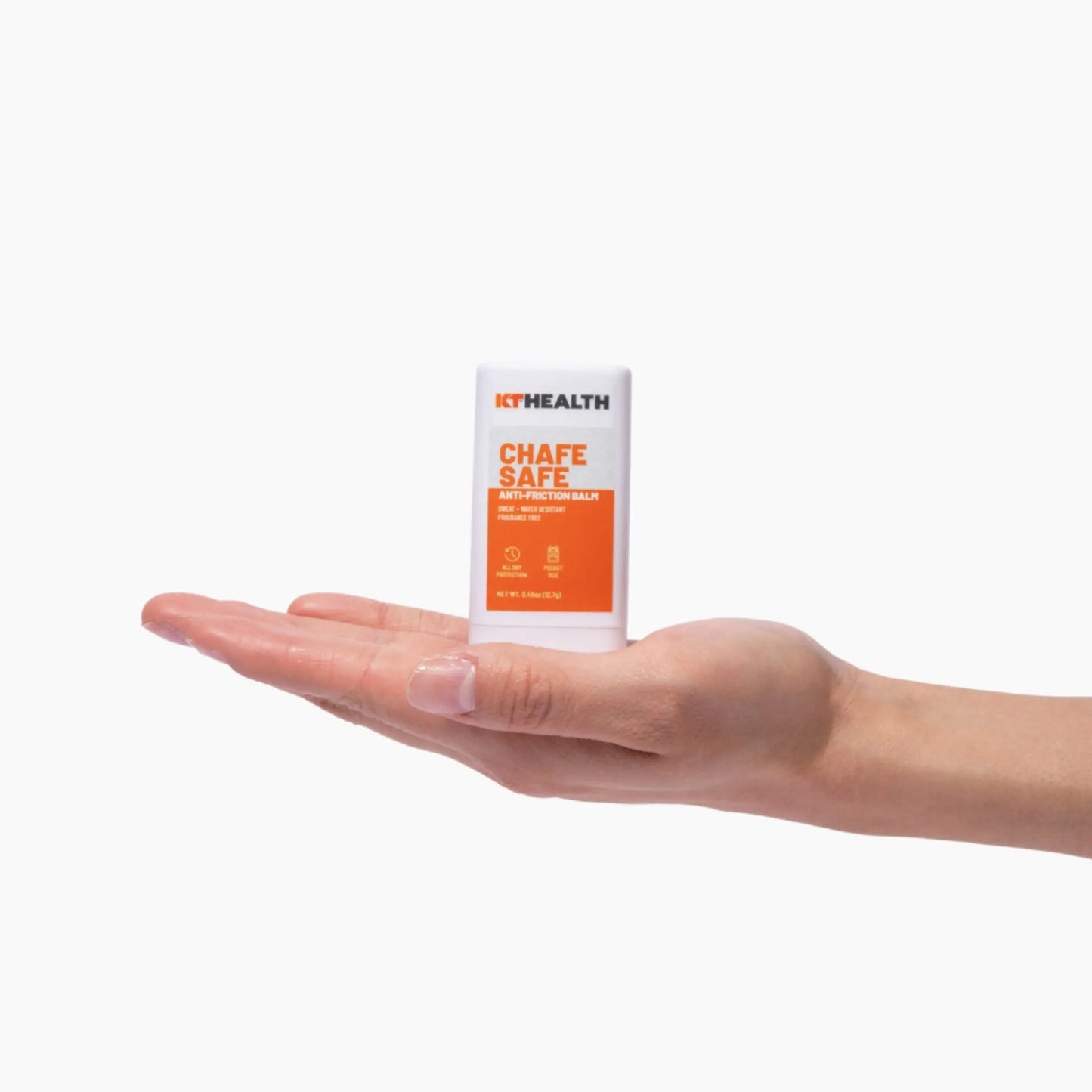 A hand with light skin holds KT Tape KT Health Chafe Safe™ Anti-Friction Balm, a small white and orange stick for chafing protection and blister prevention, centered on the open palm against a plain white background.