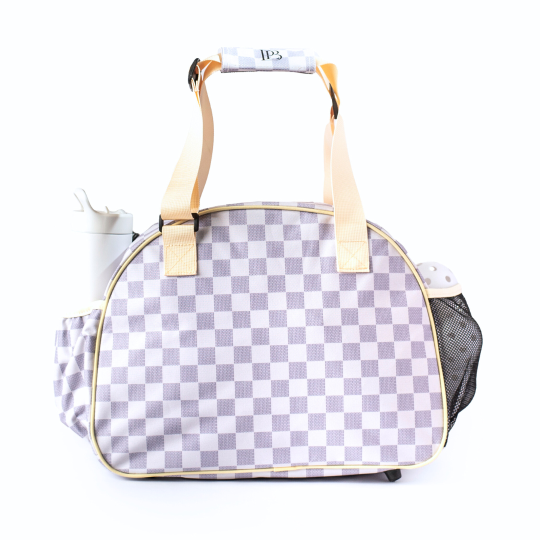 The Pik'le'Ball Sports Checkered Chic Premium Women's Pickleball Bag features light gray and white checks, beige handles, a left-side water bottle pocket, and a right mesh pocket with a white item, all set on a plain white background.