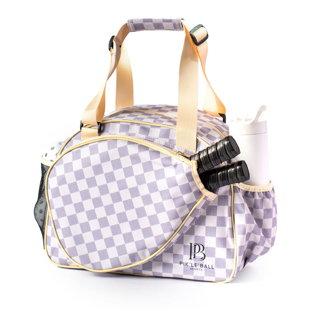 The Pik'le'Ball Sports Checkered Chic Premium Women's Pickleball Bag features lavender and white checks, beige handles, gold trim, a Pickleball logo, padded compartments, an outer pocket for two paddles and a water bottle, plus an adjustable strap.