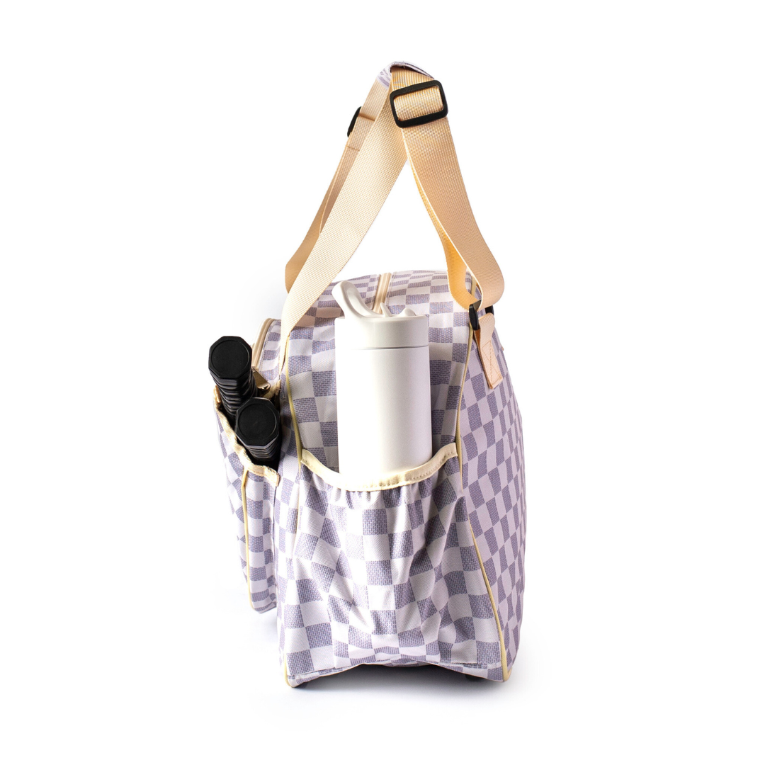 The Pik'le'Ball Sports Checkered Chic Premium Women's Pickleball Bag features lavender and white checks, beige adjustable straps, padded compartments, and exterior pockets holding a white tumbler and two containers. Shown upright on a white background.
