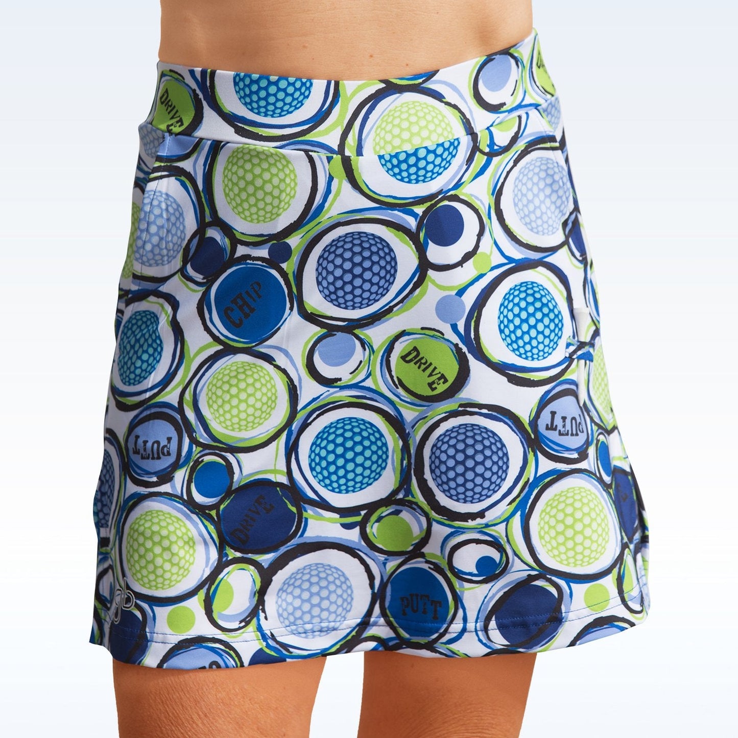 The Pickleball Bella Chip 1 Straight Golf Skort features bold blue, green, and teal golf ball circles with CHIP, DRIVE, PUTT, and LONG on a light blue background, made from 4-way stretch fabric.