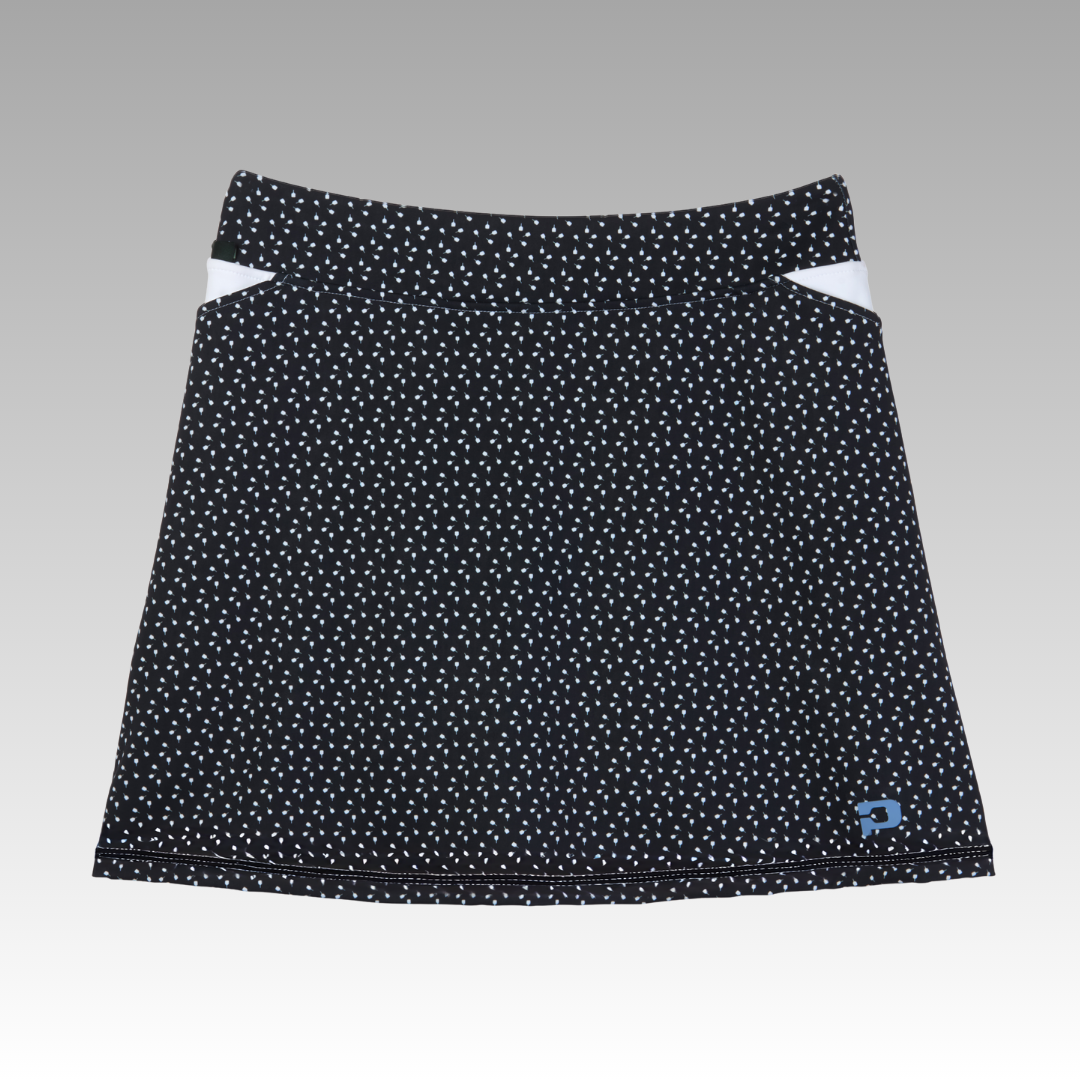 The Playly Store Sammy Skort 2.0 is a black pickleball skort with white polka dots, two white triangular accents by the waistband, and a small blue logo patch, designed to elevate your look against a gray gradient background.