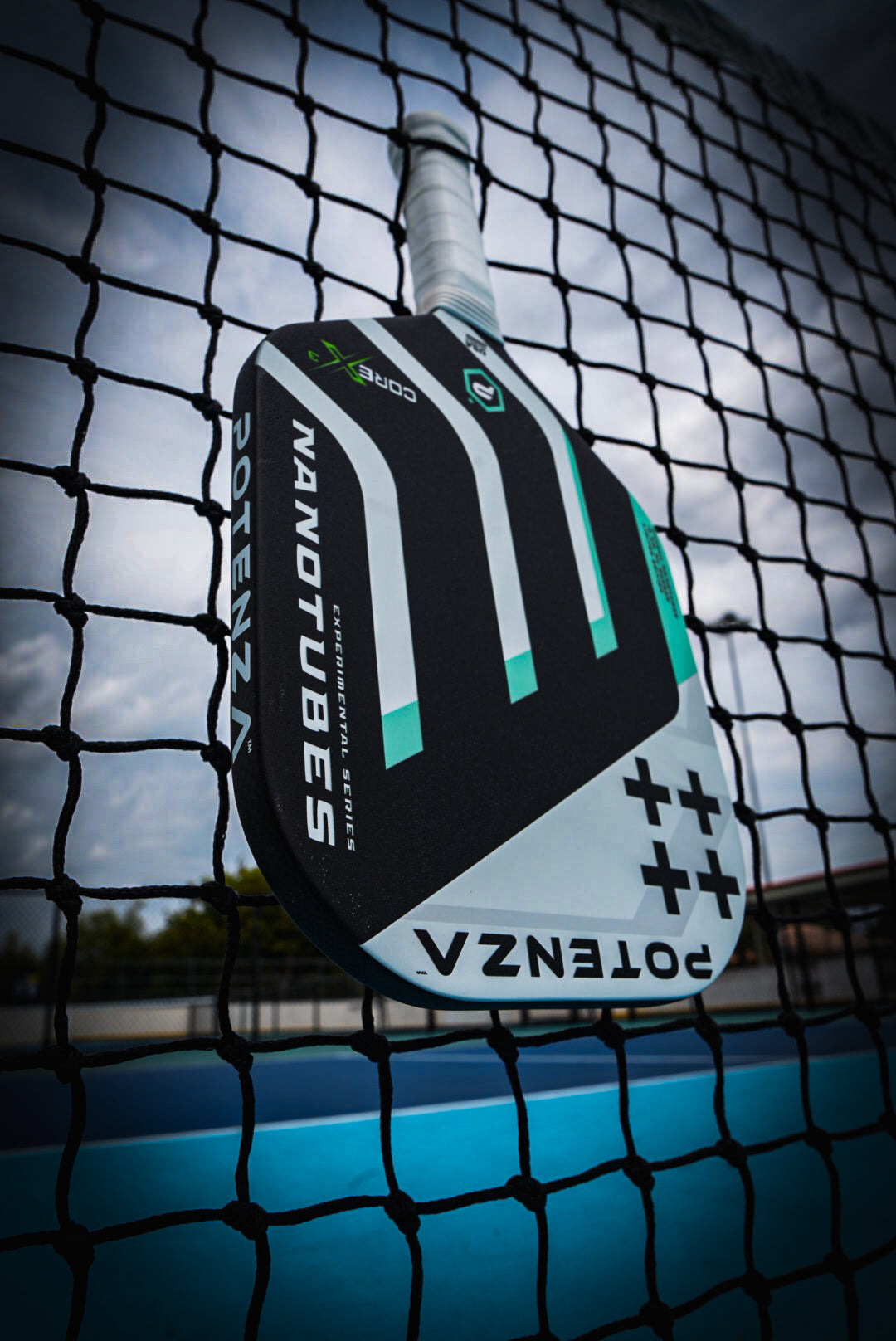 The Potenza Pickleball Carbon Nanotubes+ COREx3 paddle rests on a net, showcasing advanced COREx3 technology for superior performance.