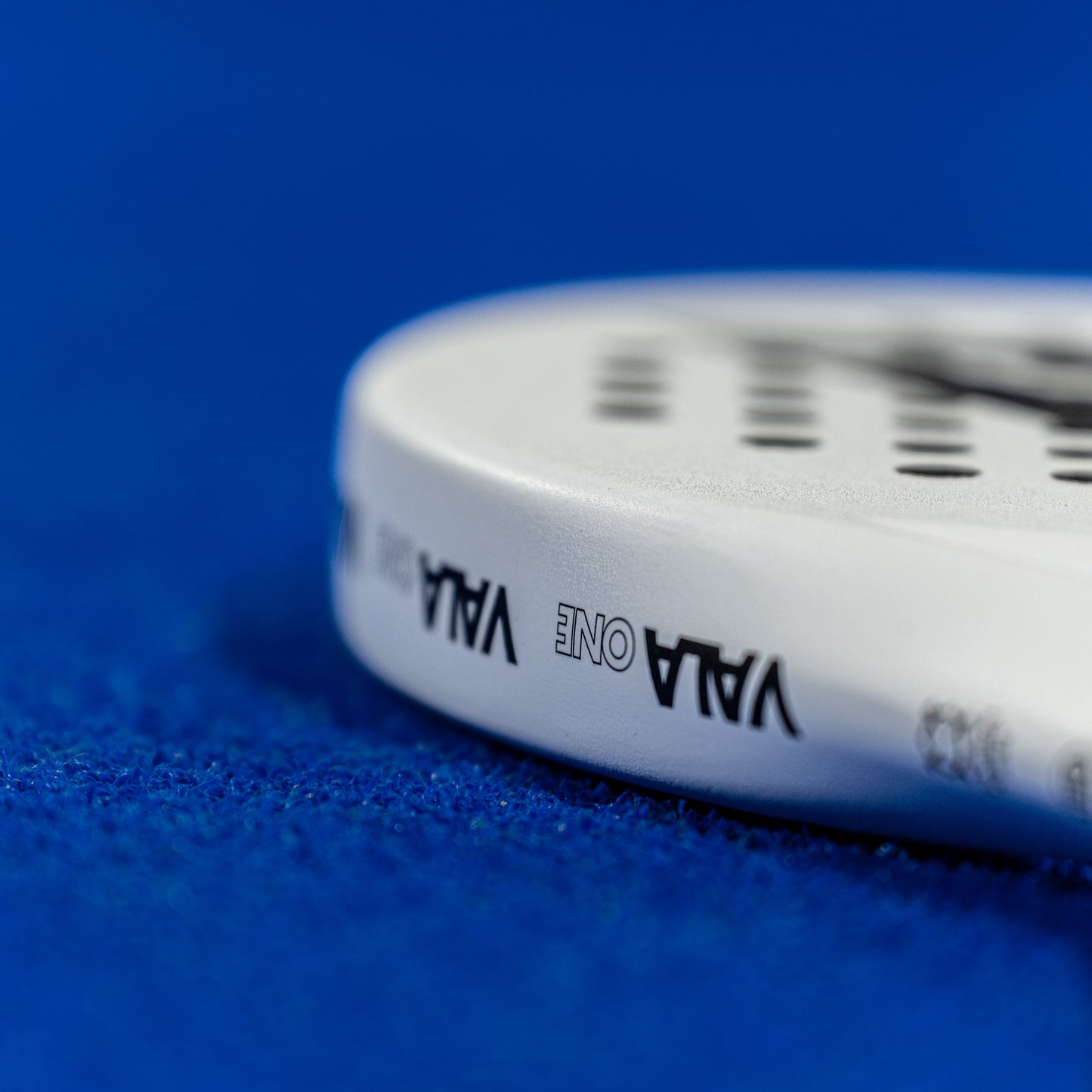 Close-up of the VALA One (White Edition) padel racquet by VALA, showcasing its branding and minimalist design against a vibrant blue textured padel court.