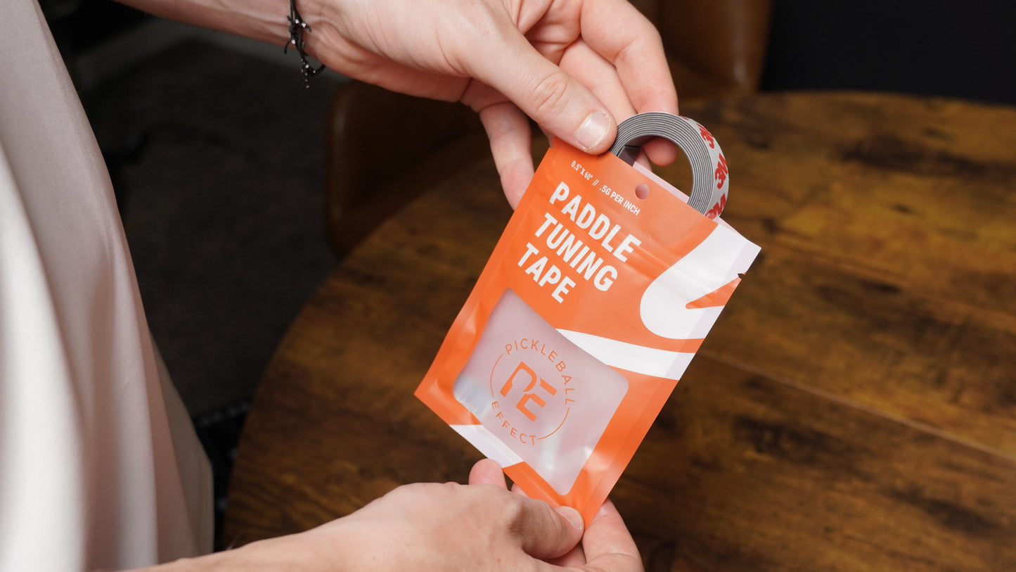 A person’s hands remove a roll of gray Paddle Tuning Tape from an orange and white Pickleball Effect Shop package. This tape is used to adjust paddle balance and customize pickleball paddle weight.