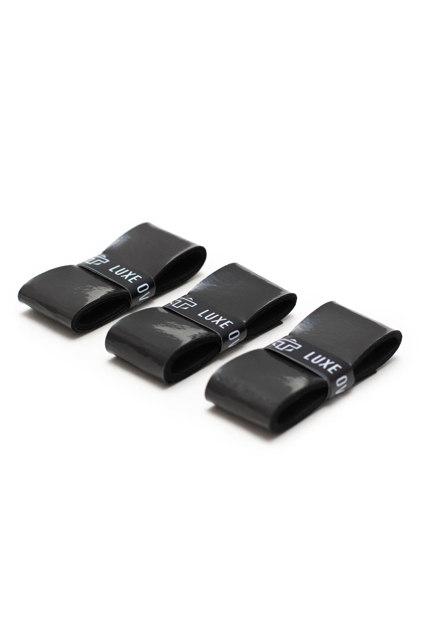 Three black TMPR Sports Luxe Tack Overgrips are neatly folded in a row on a white background, each featuring the brand name in white text and reflecting light with a glossy finish.