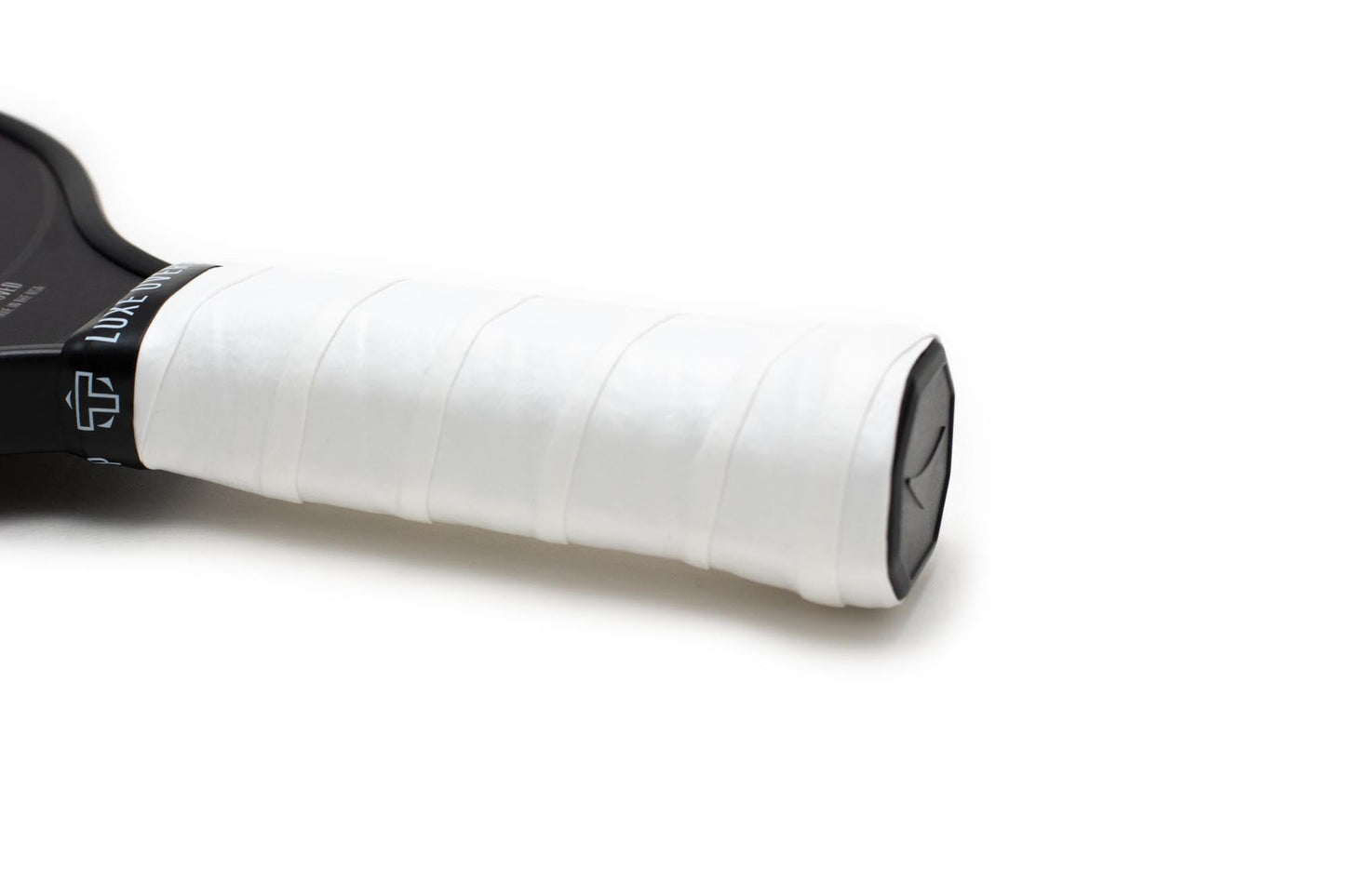 A close-up of the TMPR Luxe Tack Overgrip by TMPR Sports shows its smooth, white texture wrapped around a tennis racket handle, with the layered grip and part of the black frame displayed on a white background.