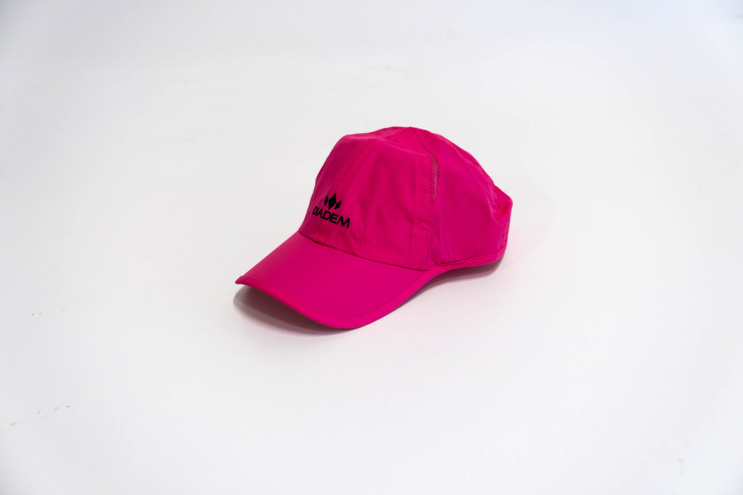 The Drycore Select Hat by Diadem Sports, in bright pink polyester, rests on a white surface. The cap features a black logo and "SADEM" on the front. Even lighting highlights its design against a plain, uncluttered background.