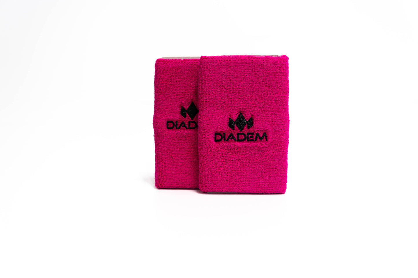 Two bright pink Diadem Logo 5" Wristbands by Diadem Sports stand upright on a white background. Each double wide, super absorbent band features a black embroidered Diadem logo and text in the center, with minimal shadows below.