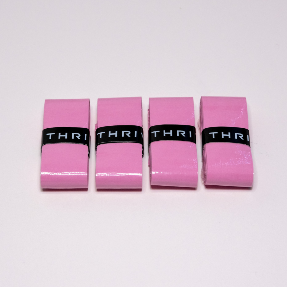 Four pink rectangular Thrive Pickleball Overgrips (Super Tacky) are lined up side by side on a white surface, each wrapped with a black band that together spells "THRI." The overgrips are glossy, durable, and uniformly shaped.