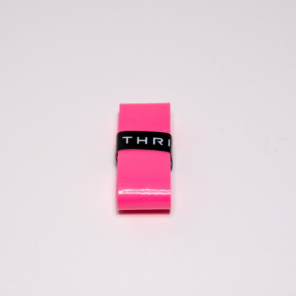 A small, shiny pink rectangular object tightly wrapped with a black band marked "THRI" is shown on a plain white background. This centered item is likely the Thrive Pickleball Overgrips (Super Tacky), photographed from above.