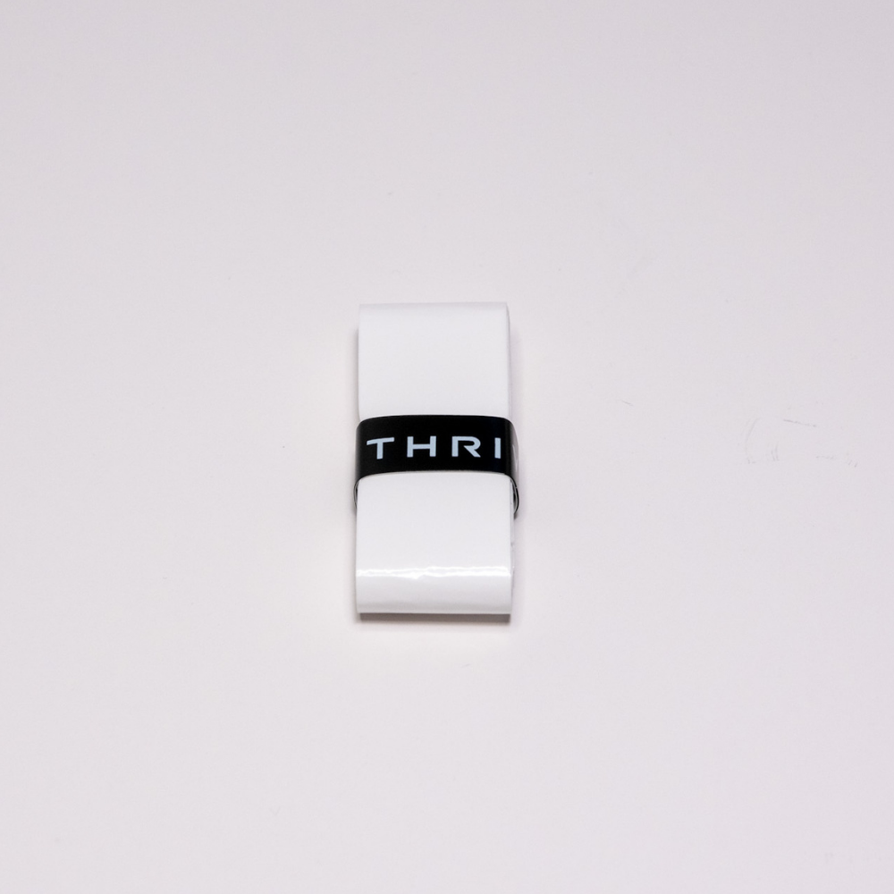 A white rectangular eraser with a black sleeve showing "THRI" in white letters rests on a light surface, its look echoing the durable Super Tacky Overgrips from Thrive Pickleball.