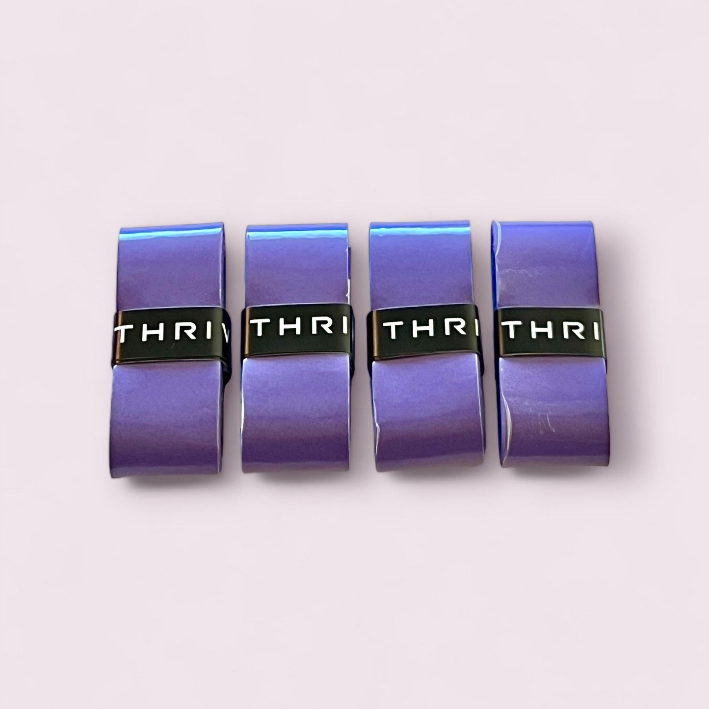 Four shiny purple Thrive Pickleball Overgrips (Super Absorbent) with black “THRI” bands are neatly aligned on a pale background. Designed for comfortable grip, these wraps absorb moisture to keep your hands dry during play.