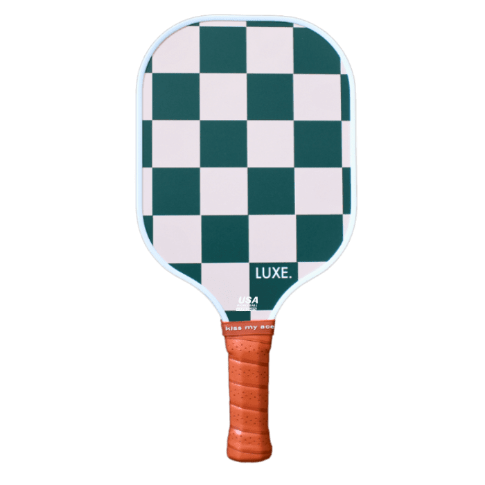 The LUXE Pickleball Checkmate paddle features a green and white checkerboard face, white border, orange-brown grip, and textured surface. "LUXE." text sits on the lower right. USA Pickleball Approved. Plain white background.