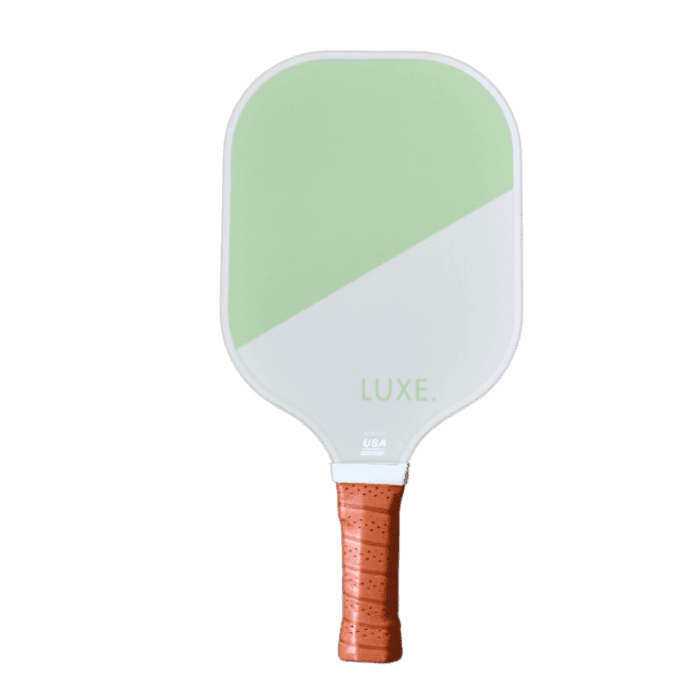 The LUXE Pickleball Dipped - Leisure paddle has a white and light green face divided diagonally, a honeycomb polymer core for durability, "LUXE." near the bottom, and a brown textured grip. It is shown on a plain light gray background.