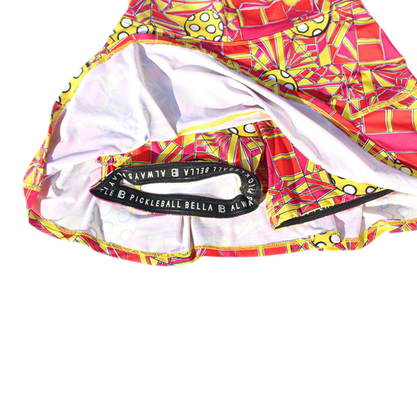 The PB Drop Pleat Skort Angle Shot 1 by Pickleball Bella features a vibrant red, yellow, and white geometric pattern, black PICKLEBALL BELLA waistband, yellow polka dot accents, white lining, and built-in compression shorts.