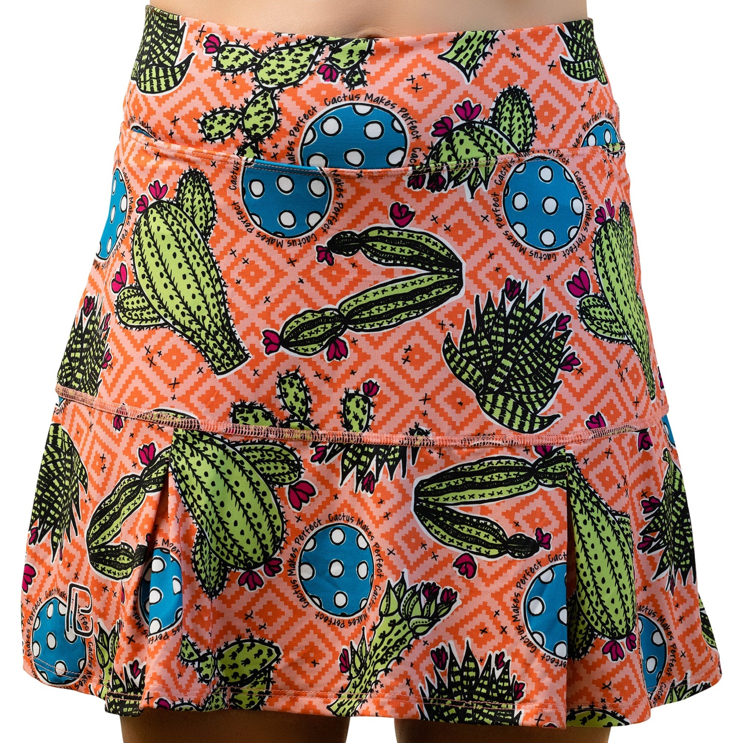 The PB Drop Pleat Skort Cactus Makes Perfect 1 by Pickleball Bella features a lively orange geometric pattern with green cactus, blue polka-dots, bottom pleats, and visible stitching—perfect for pickleball or casual wear.
