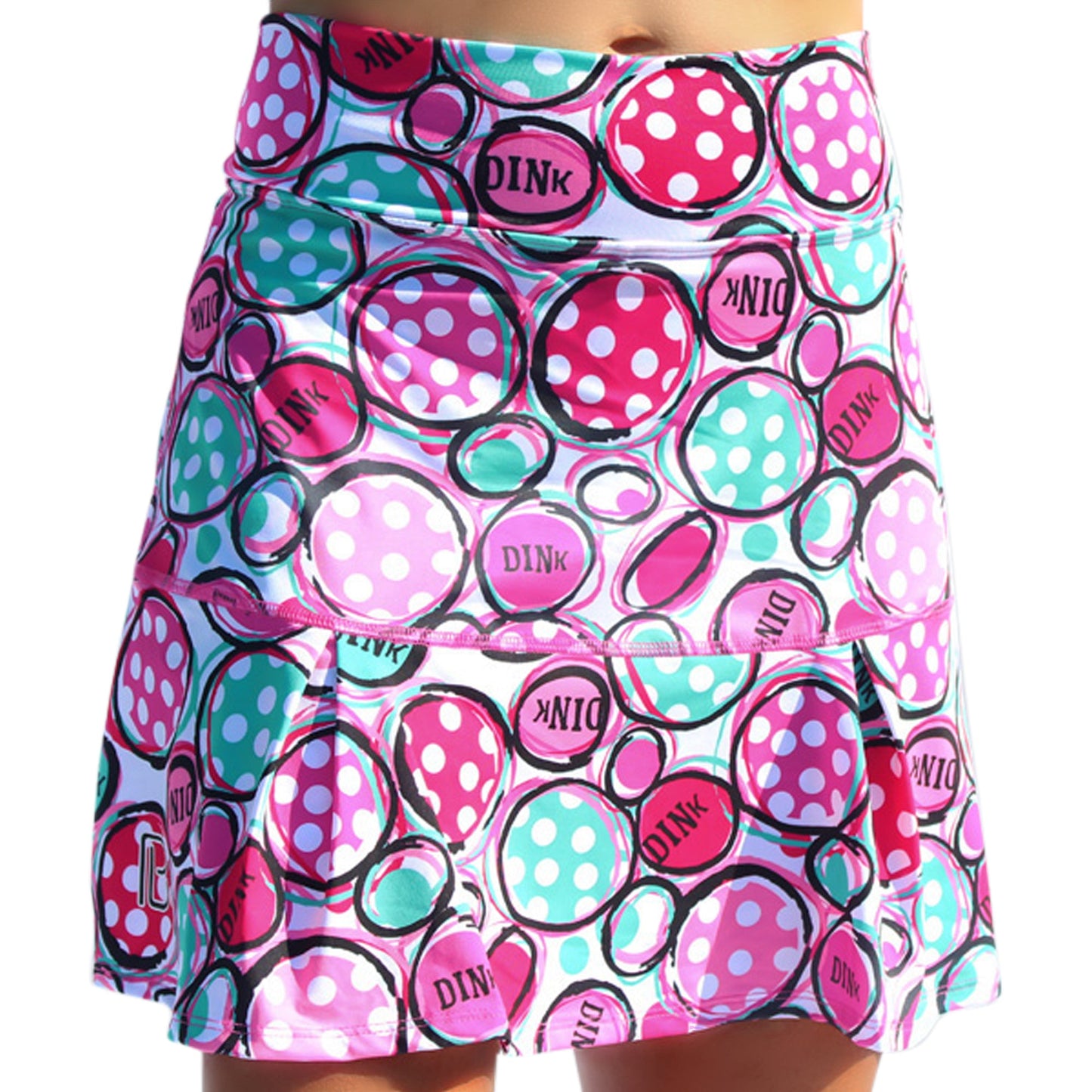 The Pickleball Bella PB Drop Pleat Skort Dink 2 features a playful pink, teal, and white pattern with circles, polka dots, and "DINK" text. Made with 4-way stretch fabric and a ball pocket, it flares out from a fitted waist for style and comfort.