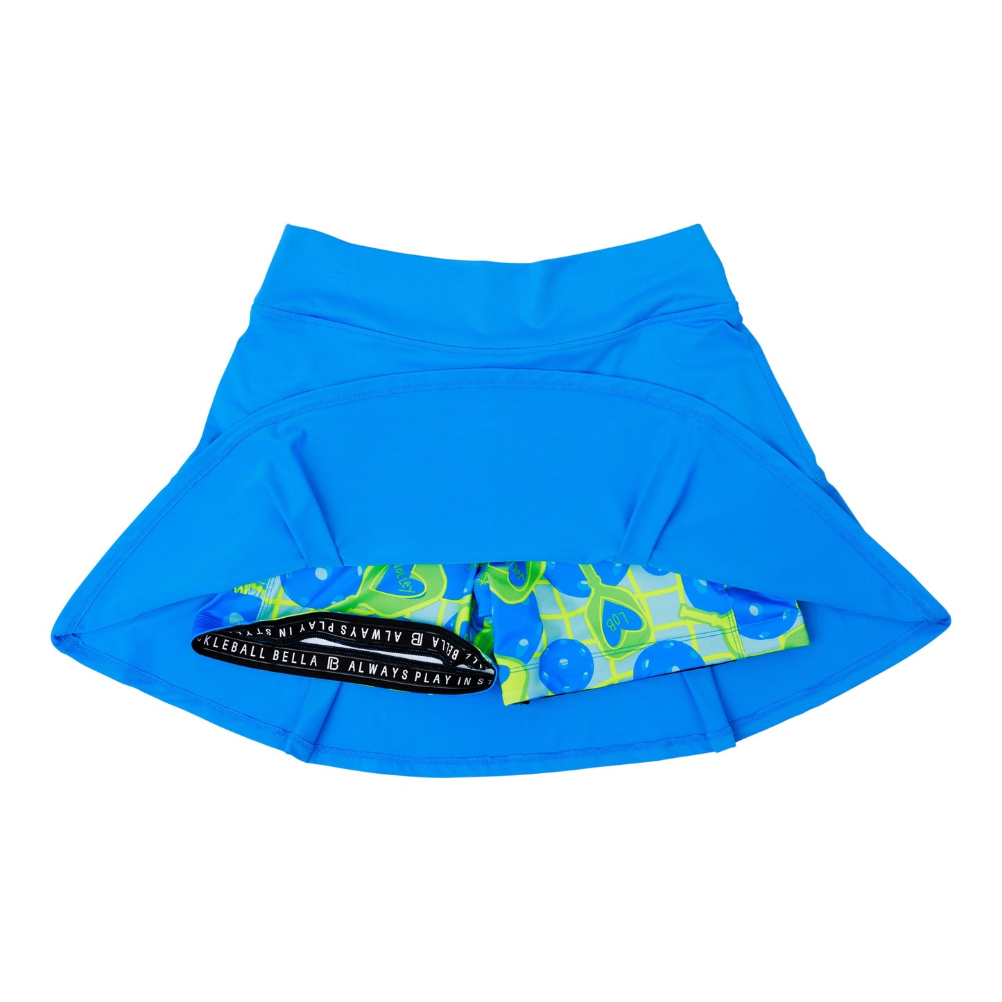 The PB Drop Pleat Skort Electric Blue with Net Worth by Pickleball Bella is shown flat with its hem lifted to reveal vibrant compression shorts featuring green, blue, and yellow pickleball motifs plus a black waistband—a sporty, stylish pickleball skirt.
