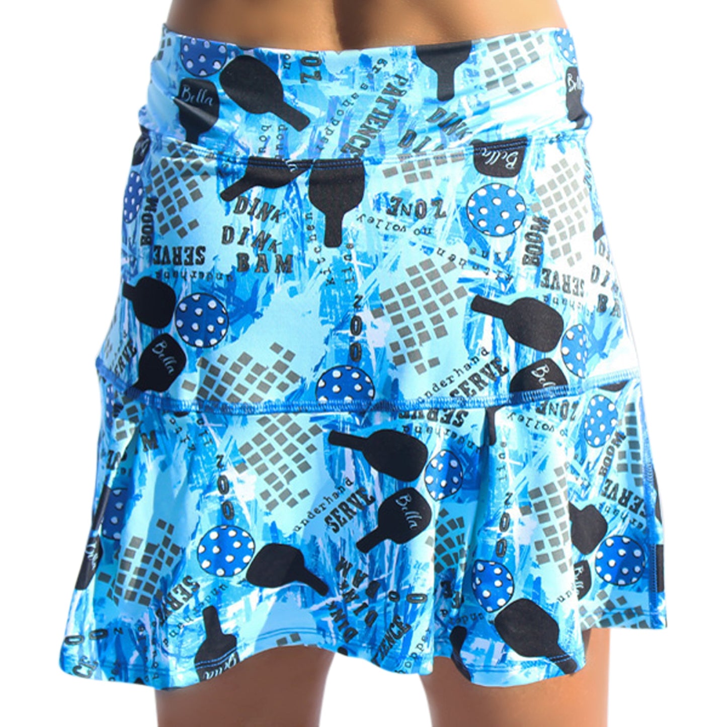 The Pickleball Bella PB Drop Pleat Skort Graffiti 2 is a blue skort with pleated ruffles, featuring black paddle prints, blue pickleballs with white dots, graffiti elements, scattered gray text, and abstract shapes on vibrant blue.