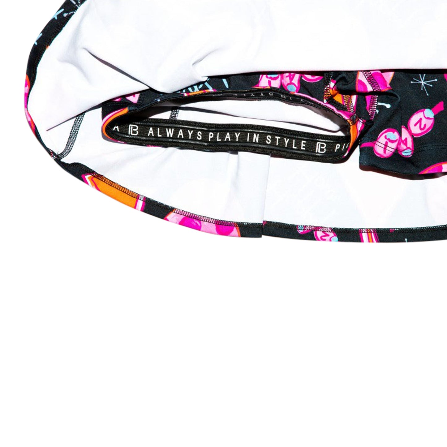 A close-up of Pickleball Bella's PB Drop Pleat Skort Martini 2-4-1 Happy Hour reveals its black waistband with “ALWAYS PLAY IN STYLE” in white and vibrant Martini Happy Hour prints in pink, orange, and purple on a black background.