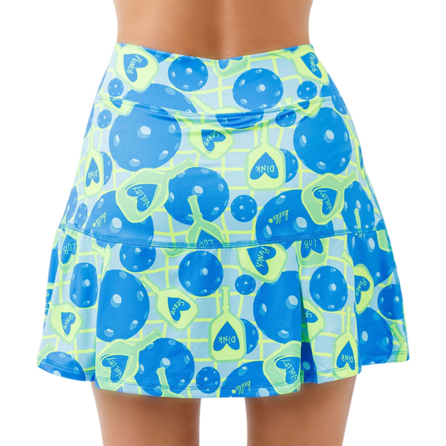 A person is shown from the back wearing the Pickleball Bella PB Drop Pleat Skort Net Worth, featuring a vibrant blue, yellow, and green pattern with large blue polka dots, yellow tennis rackets, and "PINK" in blue ovals on a lime grid.