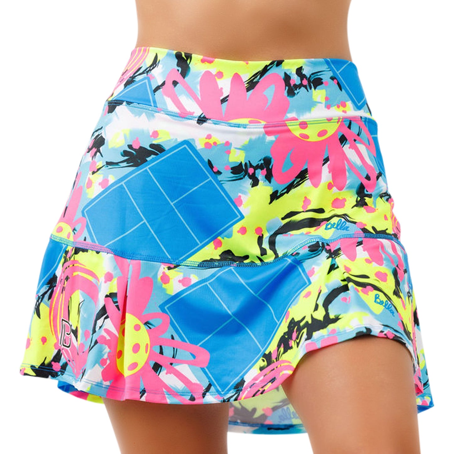 A woman wears the Pickleball Bella PB Drop Pleat Skort Open Play, a high-waisted, figure-flattering skort with a comfy waistband. Its blue rectangles, neon yellow, pink flowers, black splatters, and flared hem create a vibrant, sporty look.