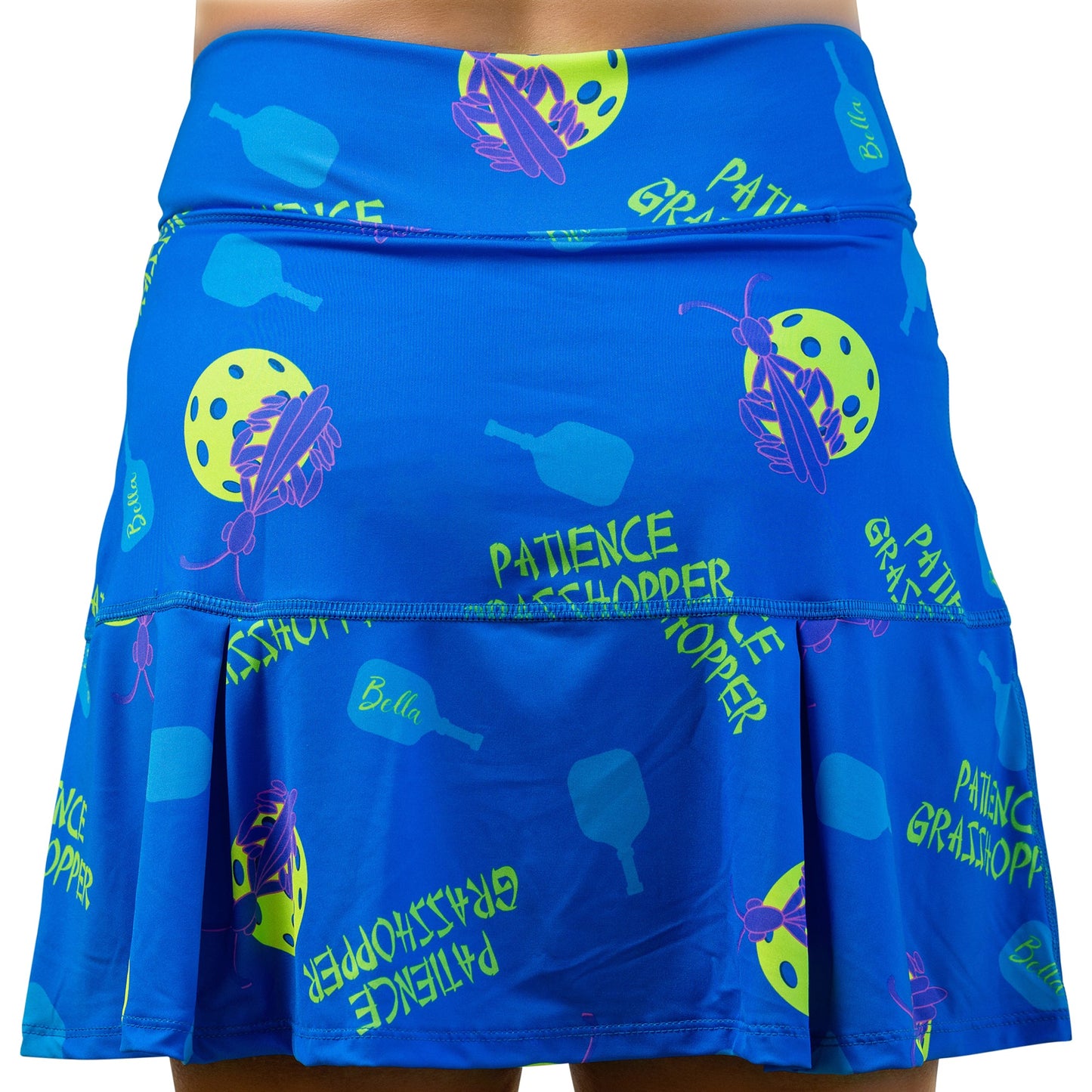 The Pickleball Bella PB Drop Pleat Skort Patience Grasshopper is a blue pickleball skirt with 4-way stretch, yellow-green “PATIENCE GRASSHOPPER” text, green paddles, purple grasshoppers, yellow pickleballs, and a flounced hem.